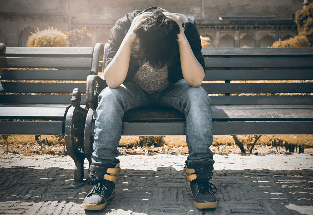 man sitting on a bench with head in hands looking depressed